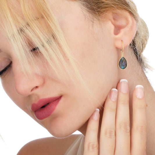 Vergoldete Silberohrringe mit Labradorit, tropfenförmiger Stein mit irisierenden Blautönen, getragen von einer Blondine.