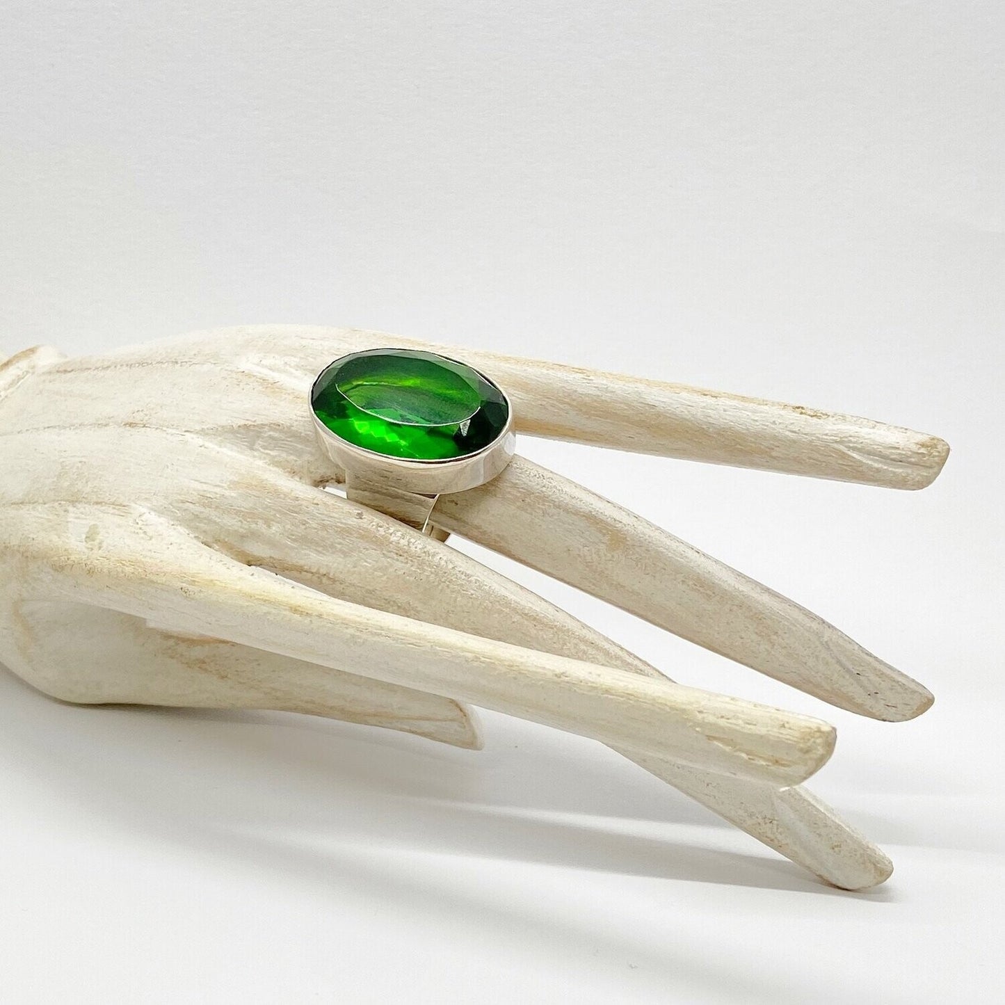 Silver ring with emerald-green obsidian oval 2x3 cm on pale sculpted wood display