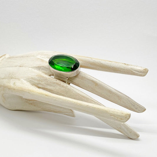 Silver ring with emerald-green obsidian oval 2x3 cm on pale sculpted wood display
