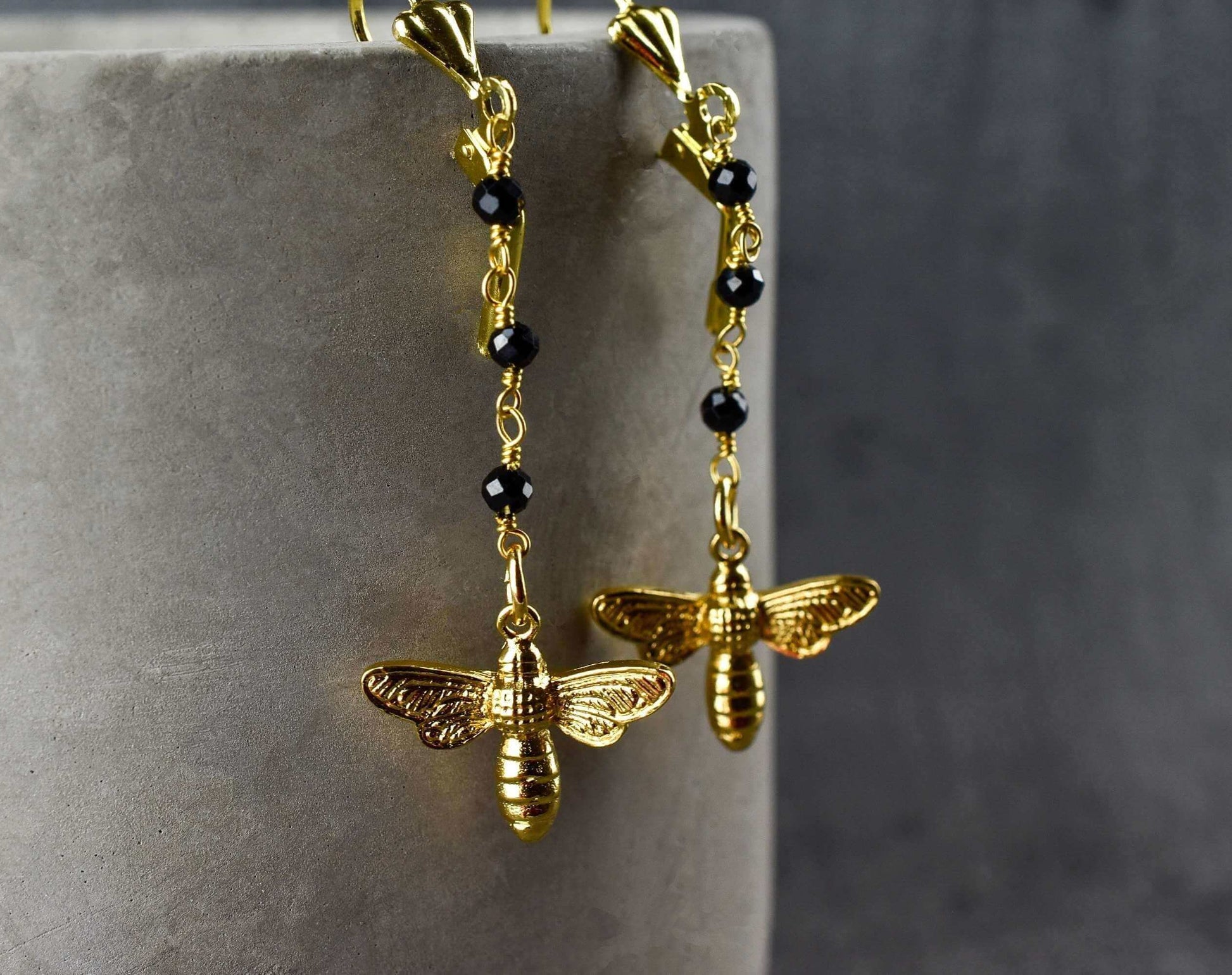 Goldene Bienen-Ohrringe mit schwarzem Onyx, filigrane Ketten mit facettierten Onyx-Kugeln.